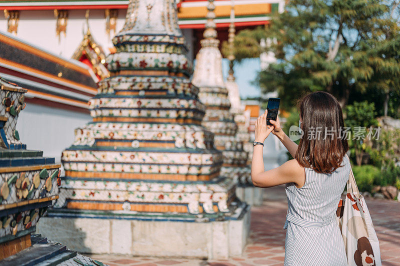 在泰国曼谷旅游胜地玉佛寺(Wat Phra Kaew)，亚洲女性游客使用智能手机享受观光